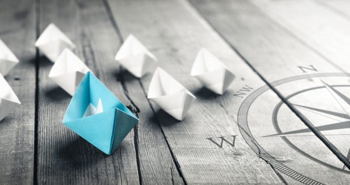 Blue Paper Boat Leading A Fleet Of Small White Boats With Compass Icon On Wooden Table With Vintage Effect - Leadership Concept